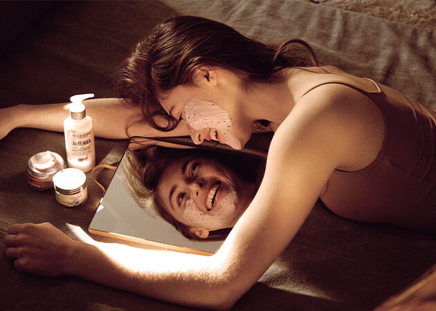 The image shows a Woman performing a skin care routine in front of a mirror