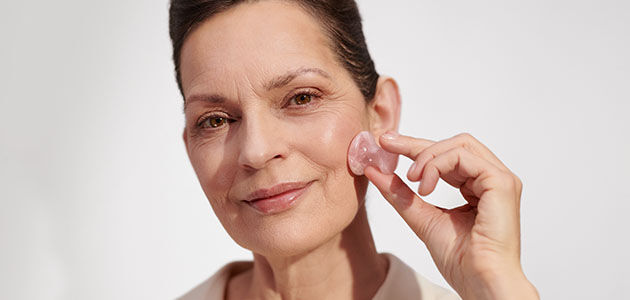 The image shows the face of an older woman gently massaging her face with the L'OCCITANE Massage tool
