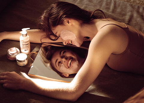The image shows a Woman performing a skin care routine in front of a mirror