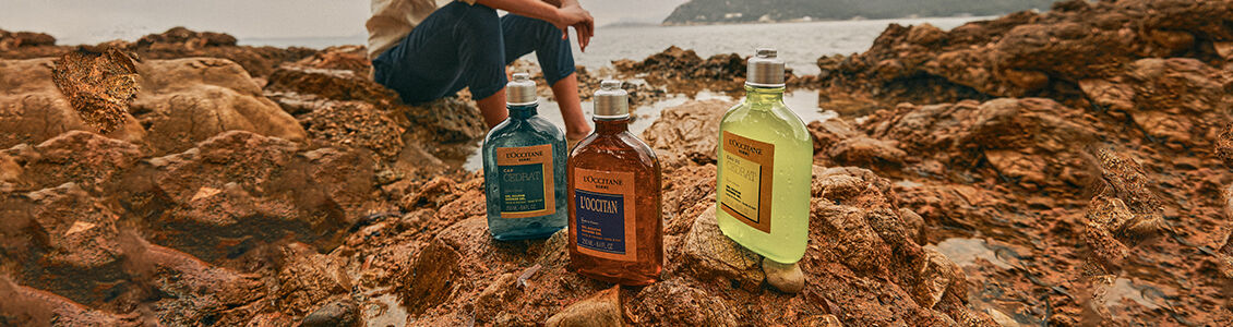 Man sitting on beach with L'OCCITANE Cap Cedrat Shower Gel, L'OCCITANE Eau de Cedrat Shower Gel & L'Occitan Shower Gel