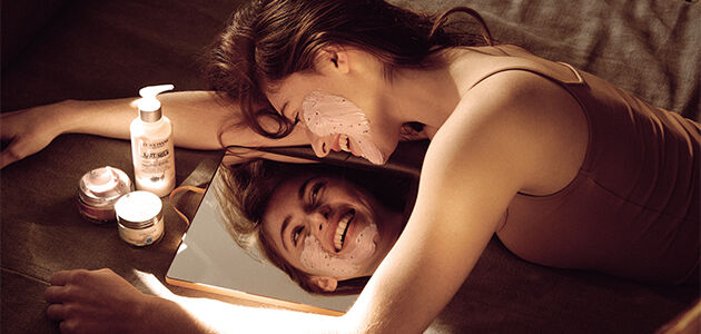 The image shows a woman performing a skincare routine in front of a mirror