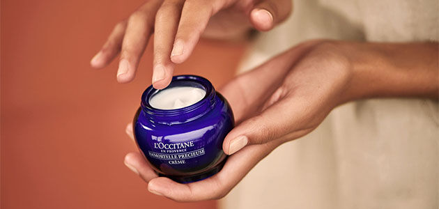 The image shows the hands of a person about to take out some of the L'OCCITANE Immortelle precious Cream